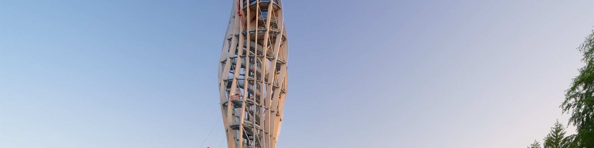 A tall, spiraling tower with a unique architectural design, surrounded by greenery and flags.