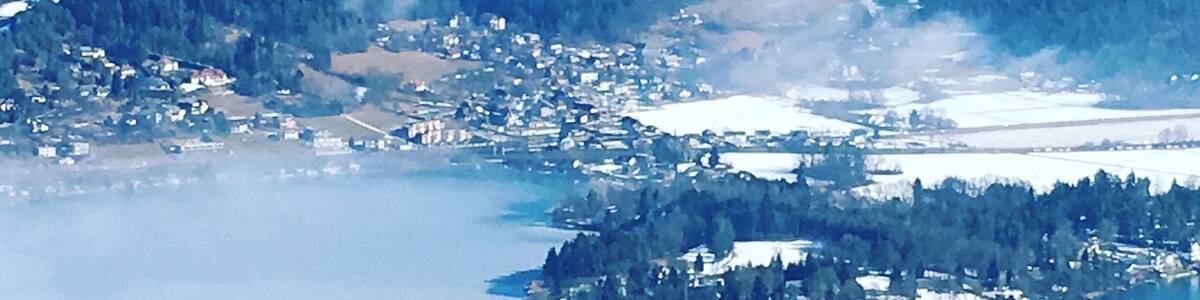 A coastal town with a church on a small island, surrounded by forested hills and a large body of water.