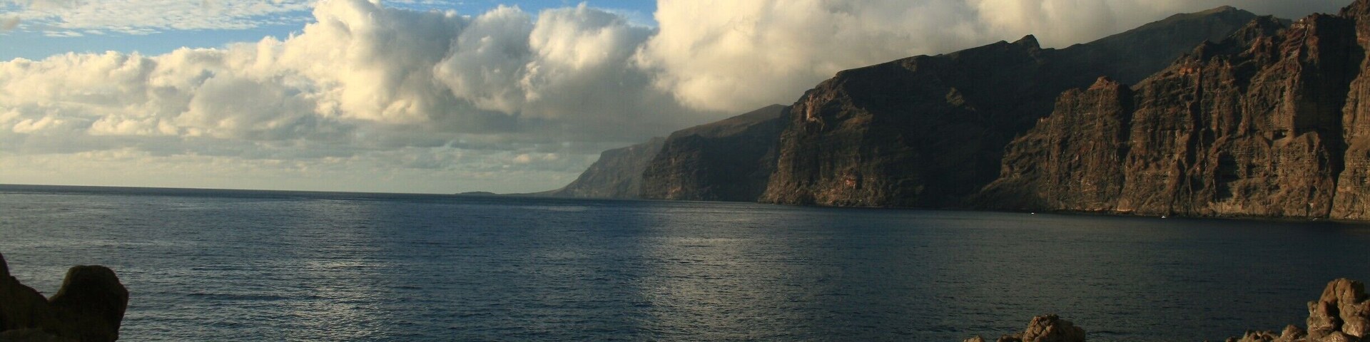 Paisagem costeira com falésias rochosas e um mar calmo sob um céu parcialmente nublado.