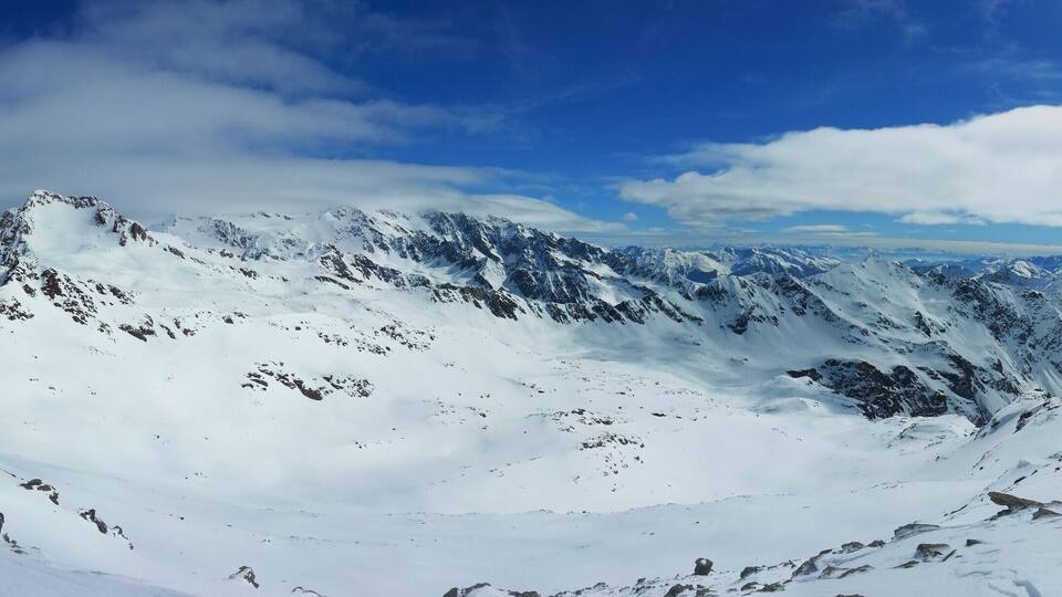 A snow-covered mountain range with rocky outcrops and a clear blue sky.