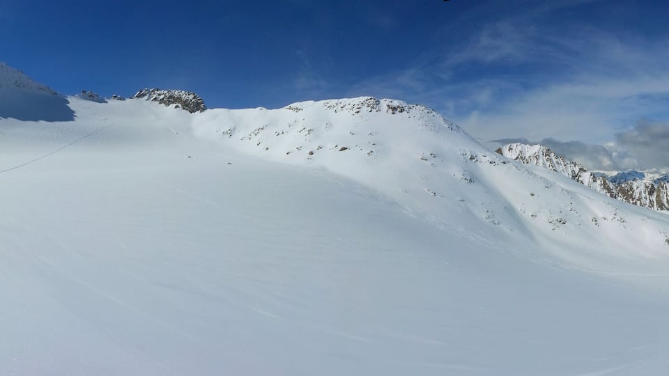 A snow-covered mountain slope with a clear sky and distant peaks.