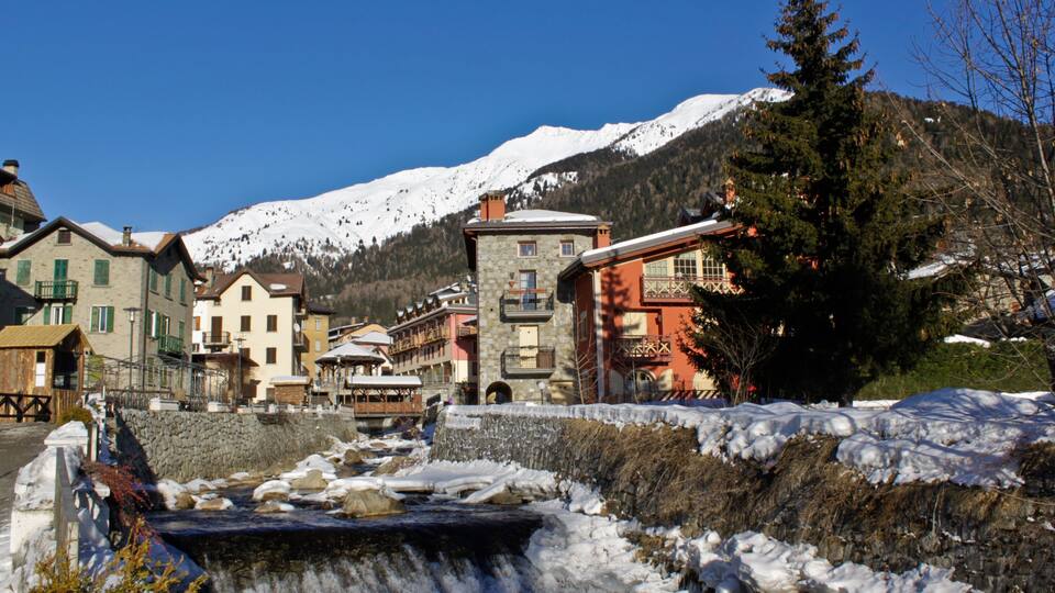 A snow-covered mountain, a flowing river, and buildings in a town.