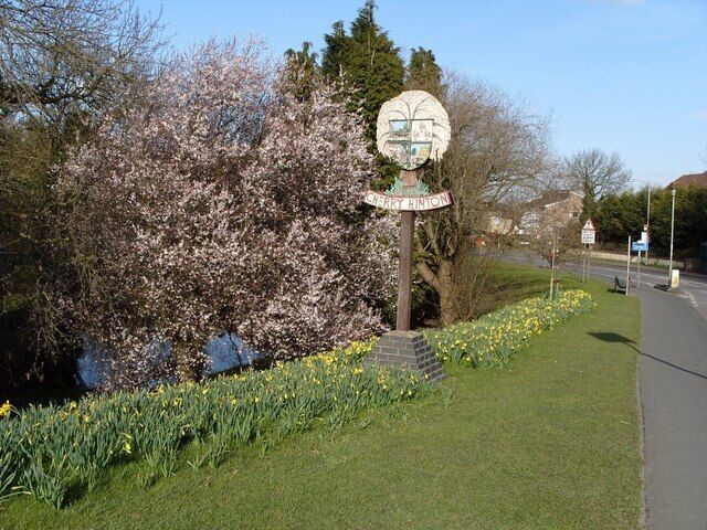 Cherry Hinton Village Sign The village sign is opposite the Robin Hood and Little John pub, and the Giants Grave pond is just visible through the trees. The sign is surrounded by a lovely display of daffodils, in the spring.