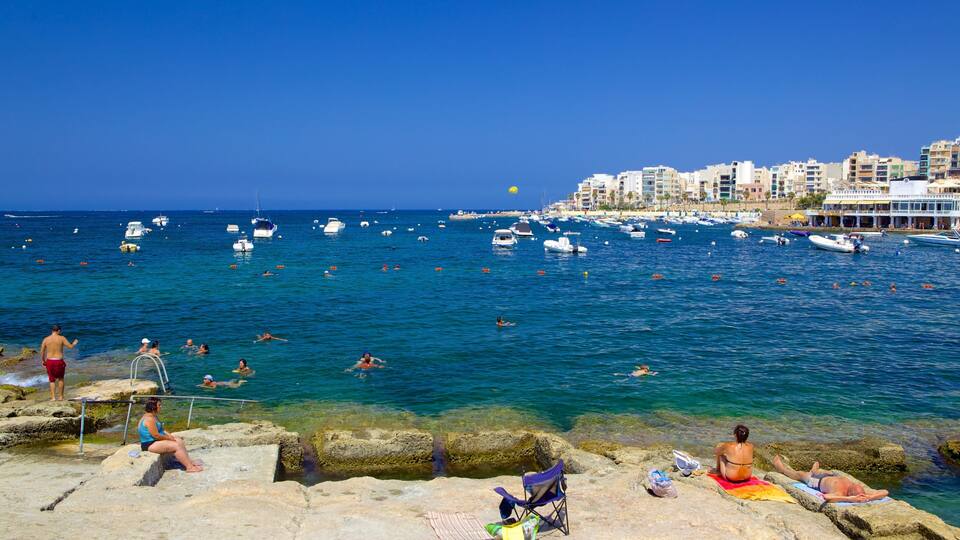 A coastal town with clear blue waters, people swimming and sunbathing, and numerous boats anchored in the harbor.