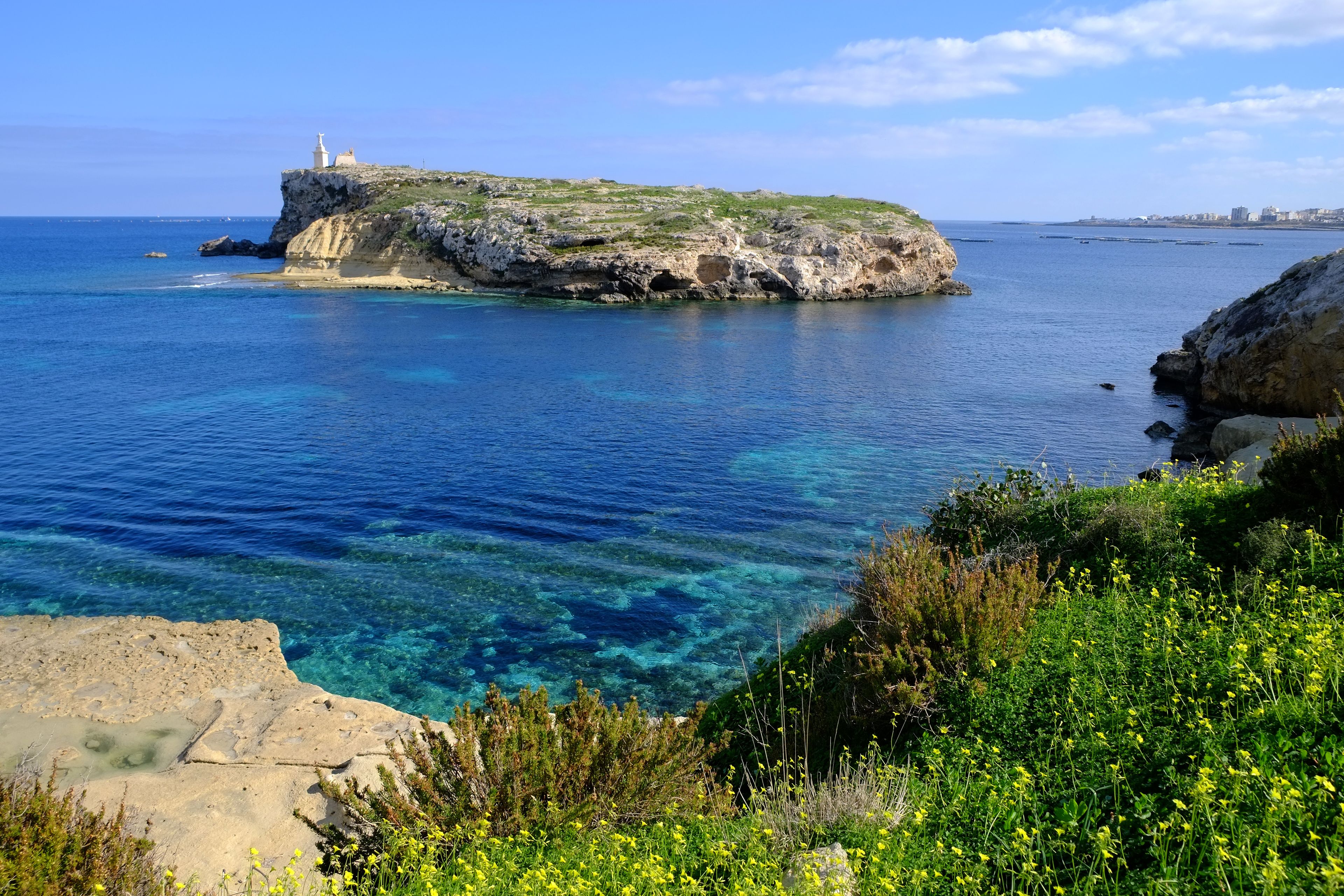 A coastal landscape with clear blue waters, rocky cliffs, and a lighthouse on a small island.