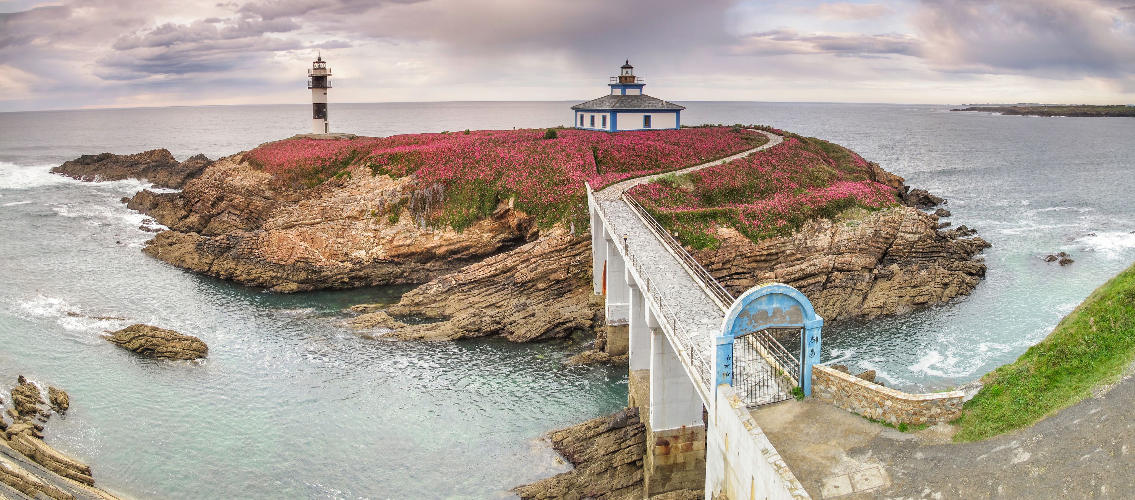 A coastal landscape with a rocky island, a lighthouse, a pier, and a bridge.