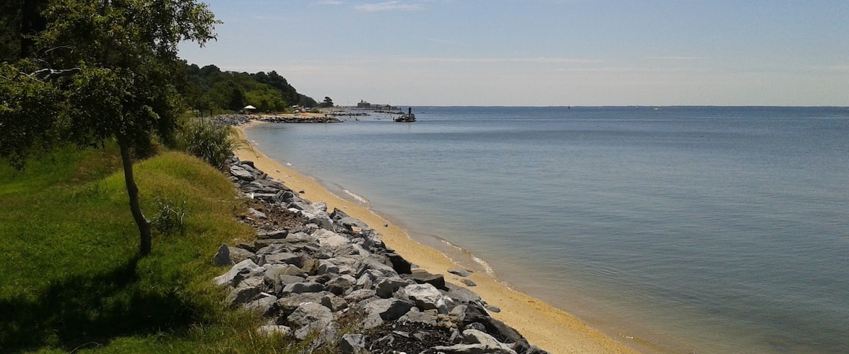 A coastal landscape with a rocky shoreline, a sandy beach, and a clear blue sky.