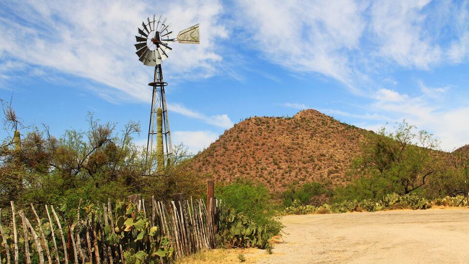 A windmill, a dirt road, and a hill with sparse vegetation.