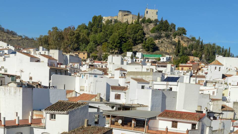 A densely packed hillside town with white buildings and a historic castle on a hilltop.