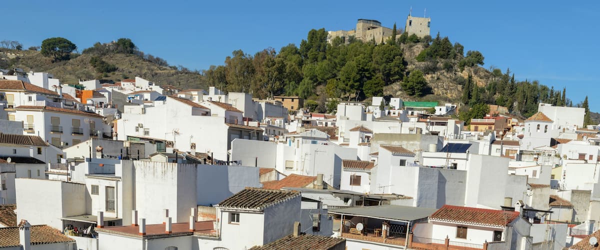 A densely packed hillside town with white buildings and a historic castle on a hilltop.