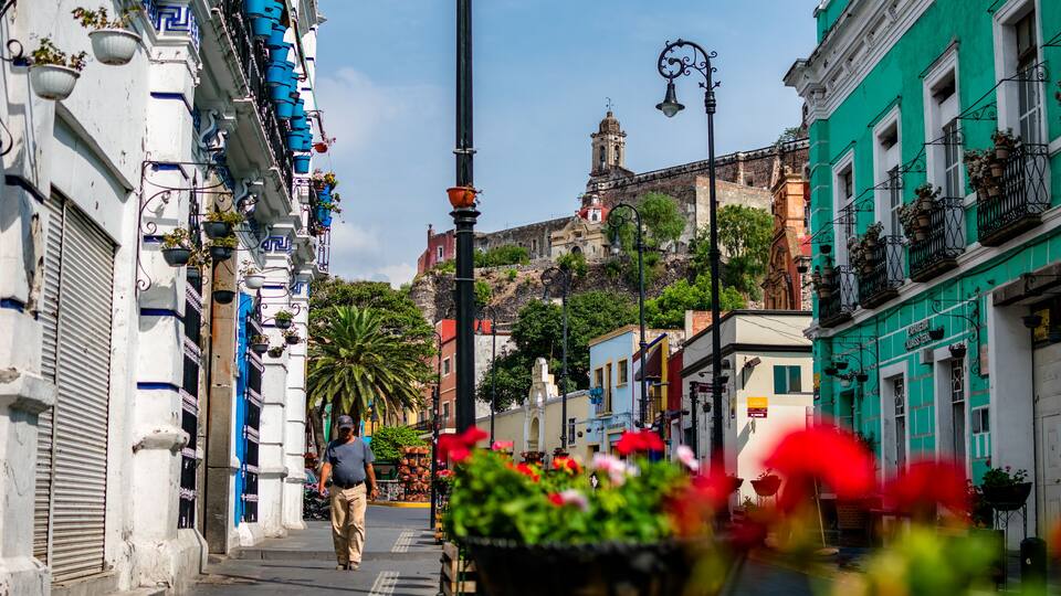 A narrow street lined with colorful buildings, a man walking, and a bell tower in the background.