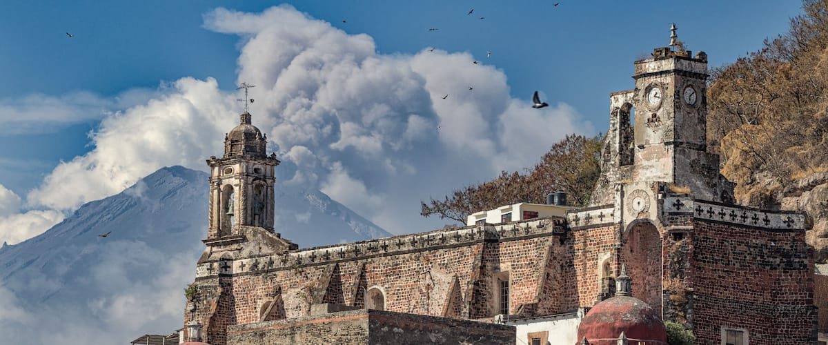 A historic church with a bell tower and a mountain in the background.
