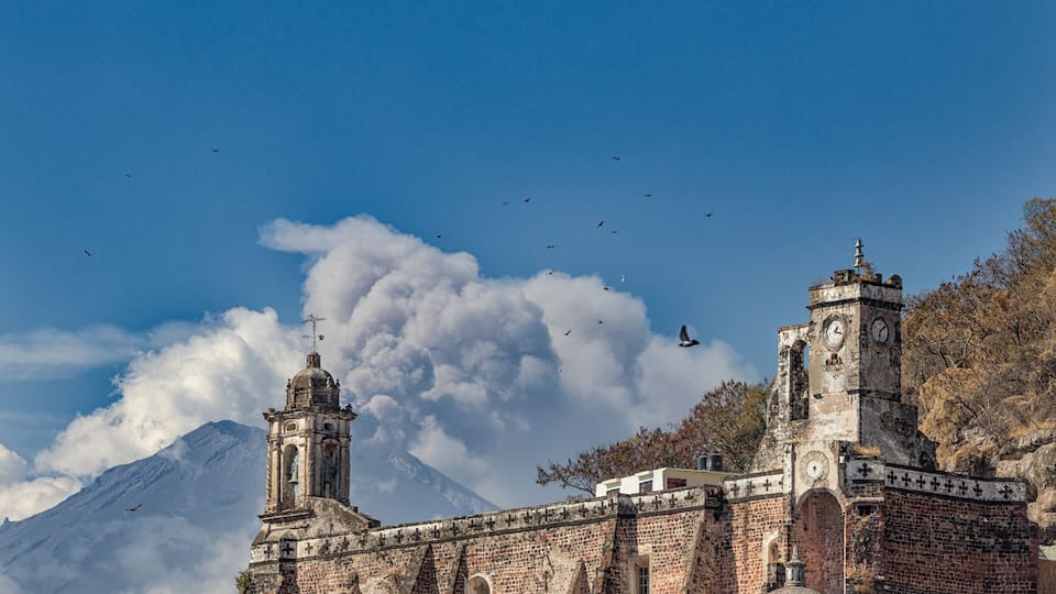 A historic church with a bell tower and a mountain in the background.