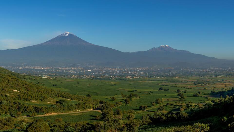 A mountain with a snow-capped peak and a valley with fields and a town in the foreground.
