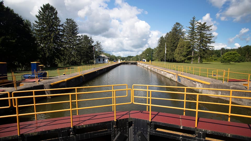 A canal with yellow railings, surrounded by trees and a clear sky.