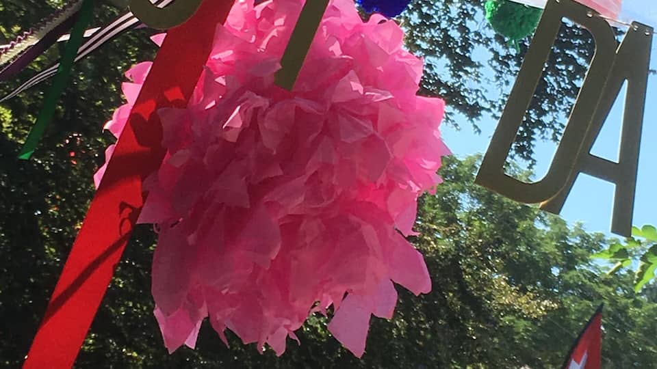 A pink piñata hanging from a red and green banner with the word "FESTA" visible.