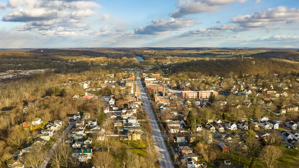 An aerial view of a small town with a river, surrounded by hills and trees.