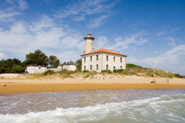 Un faro su una spiaggia sabbiosa, con le onde che si infrangono in primo piano.