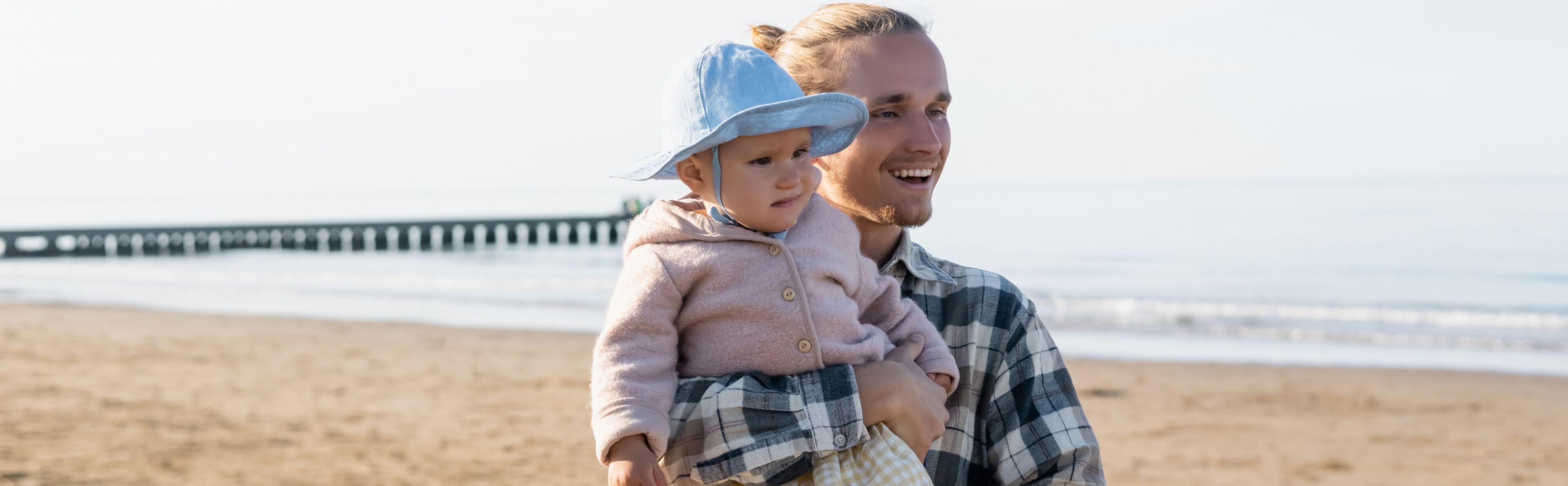 Smiling parent holding toddler kid on beach near adriatic sea in Italy, banner.