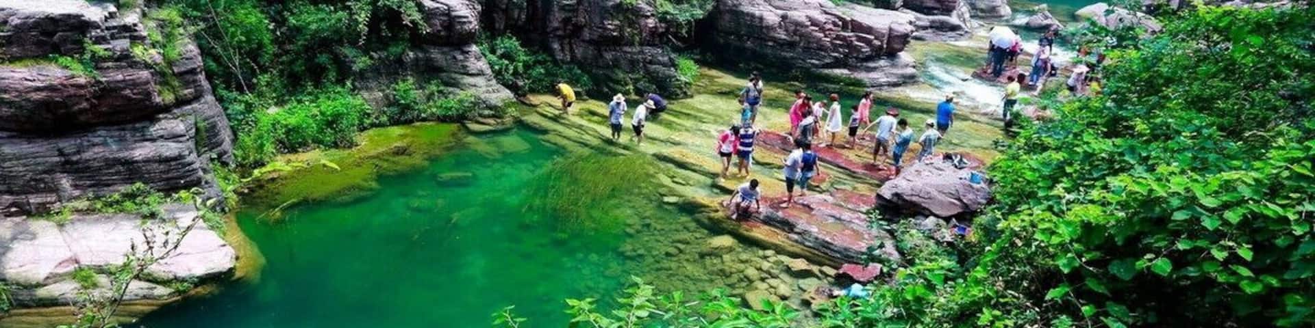 A canyon with clear water, rocky formations, and people hiking.