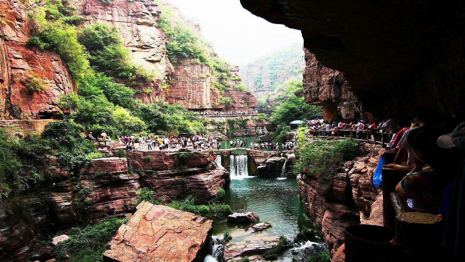 A canyon with a waterfall, a viewing platform, and people observing the scenery.
