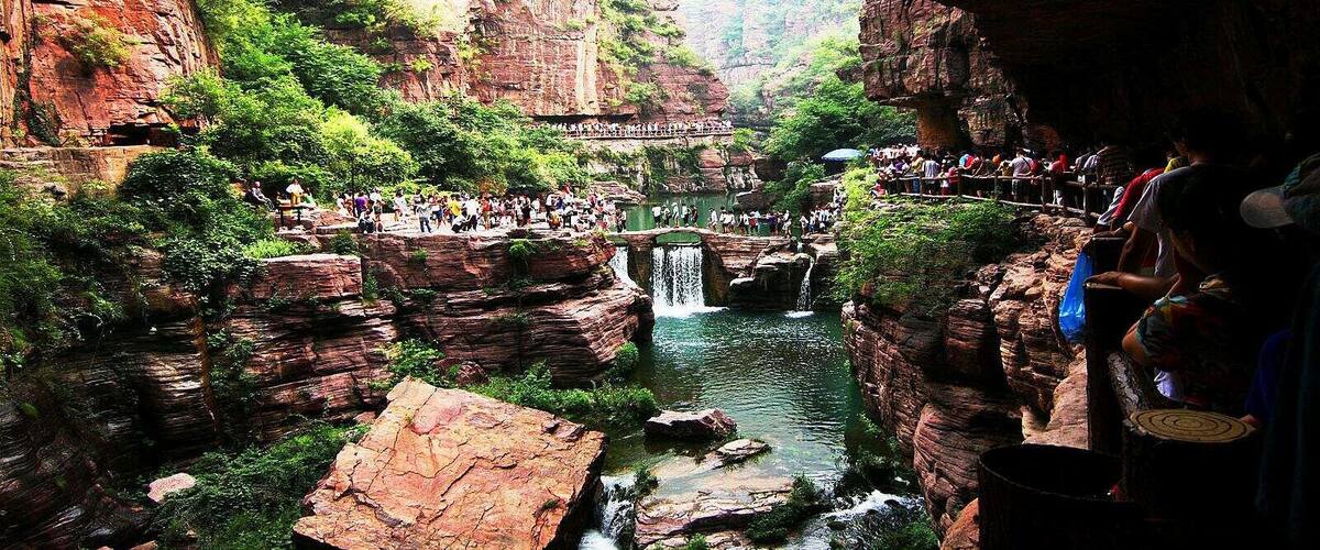 A canyon with a waterfall, a viewing platform, and people observing the scenery.