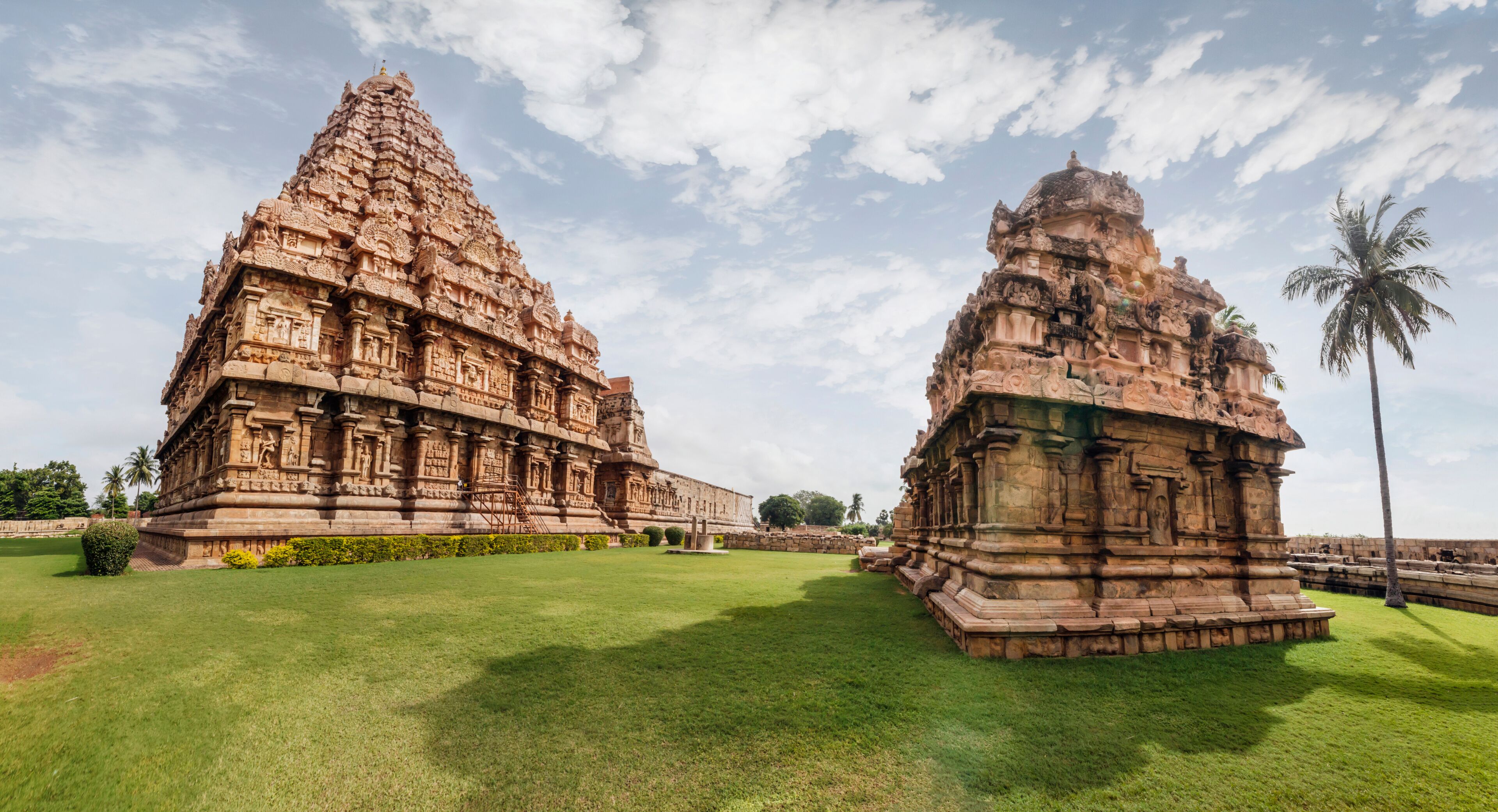 Two intricately carved temple structures with detailed stonework and a well-maintained lawn in the foreground.