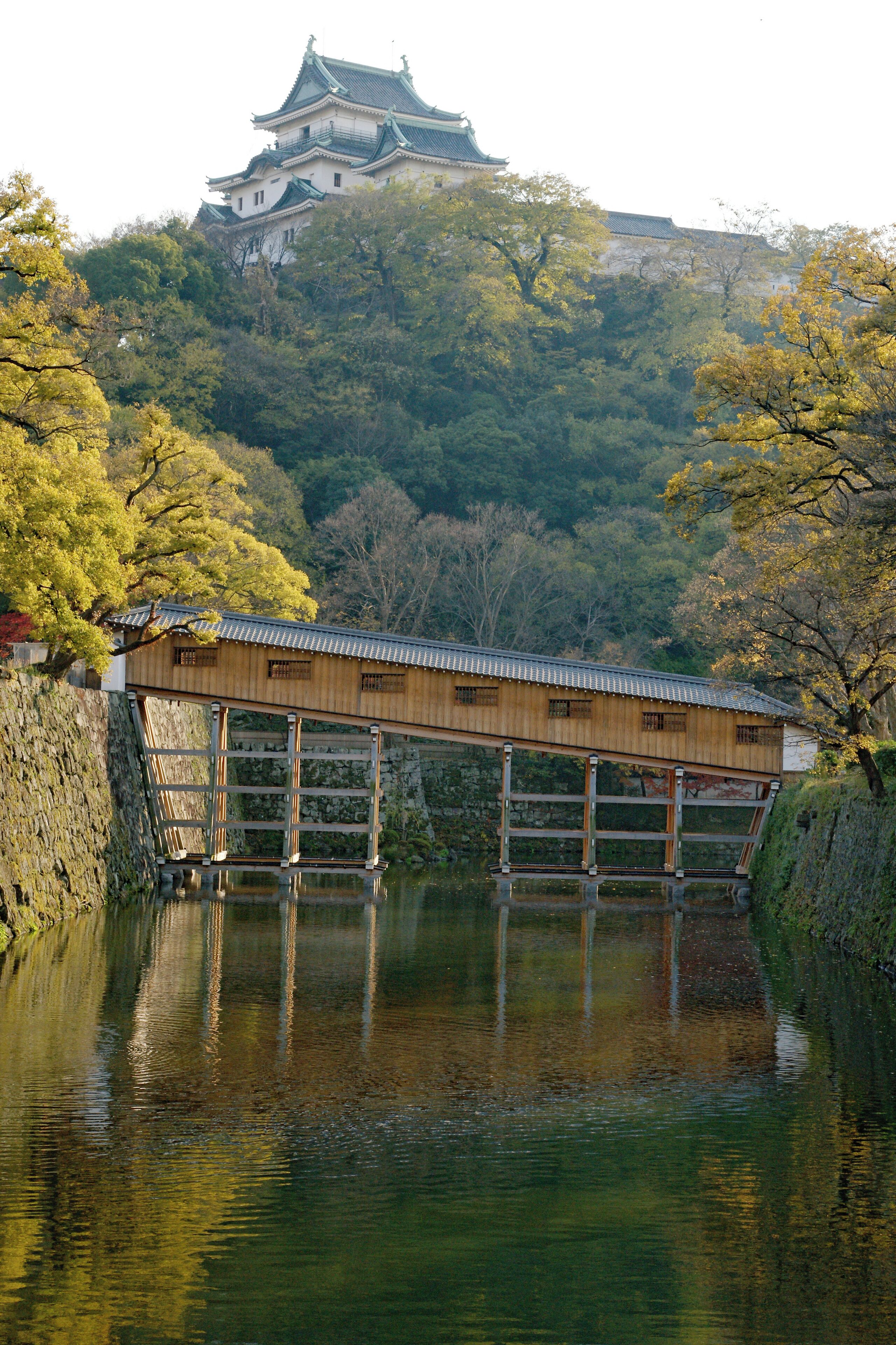 A wooden bridge over a calm river, with a traditional castle in the background.