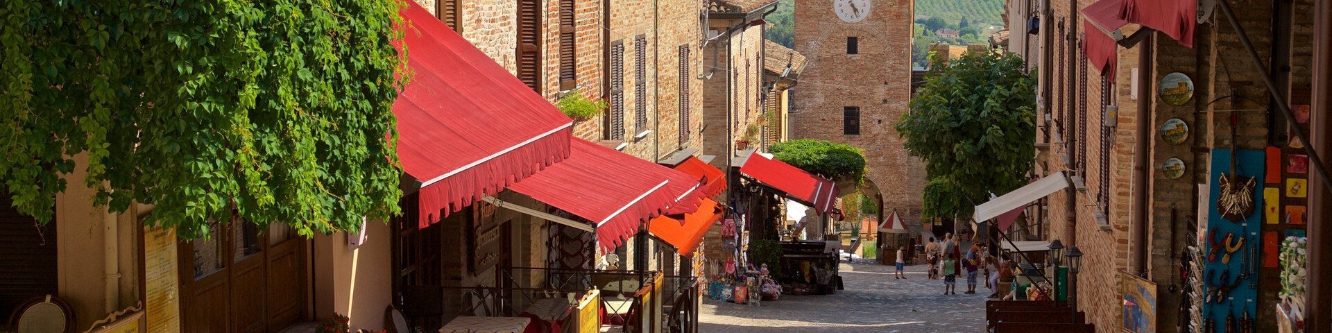 A cobblestone street lined with traditional buildings, red awnings, and a clock tower in the distance.