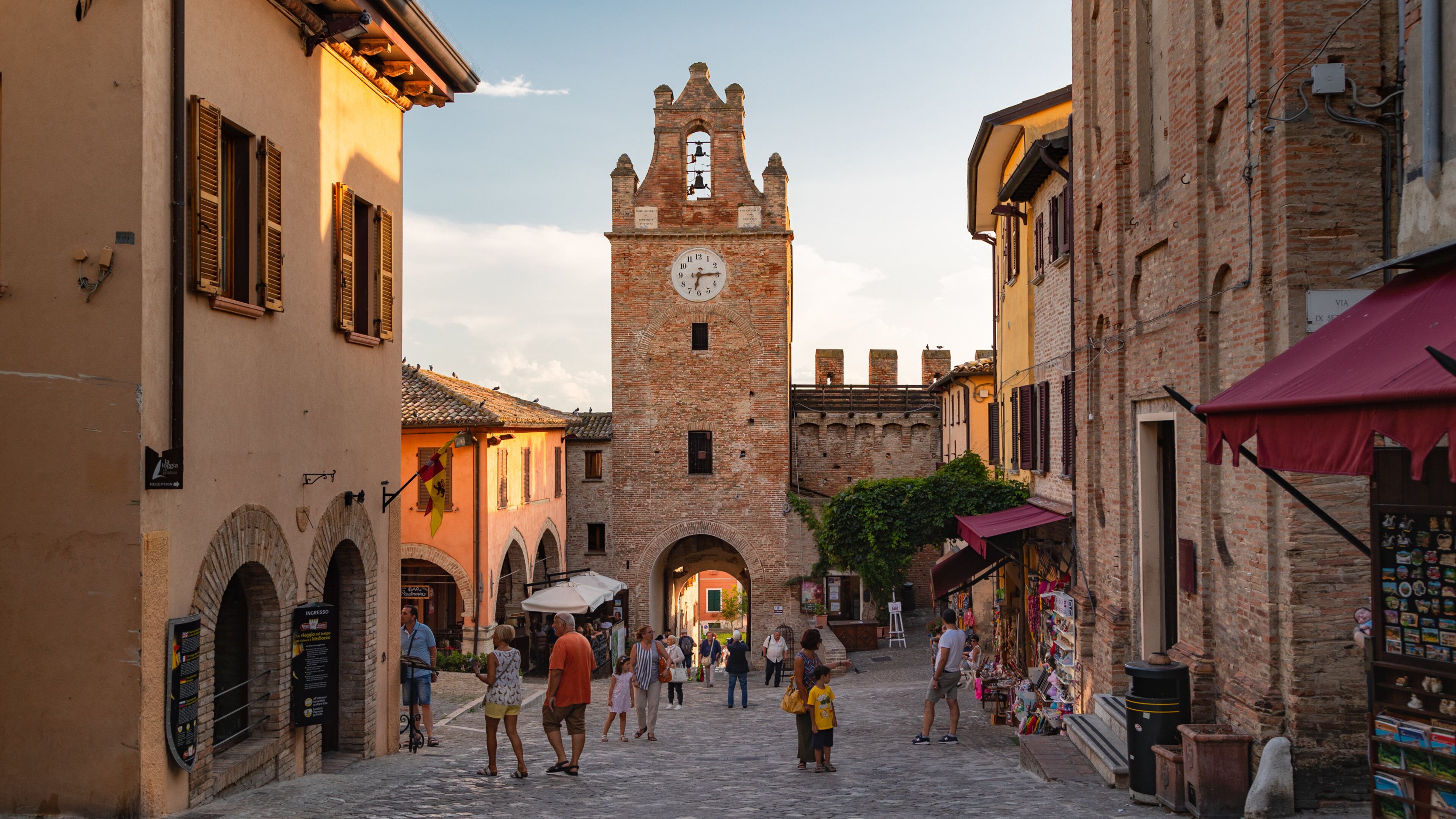 A cobblestone street with historic buildings, a clock tower, and people walking.