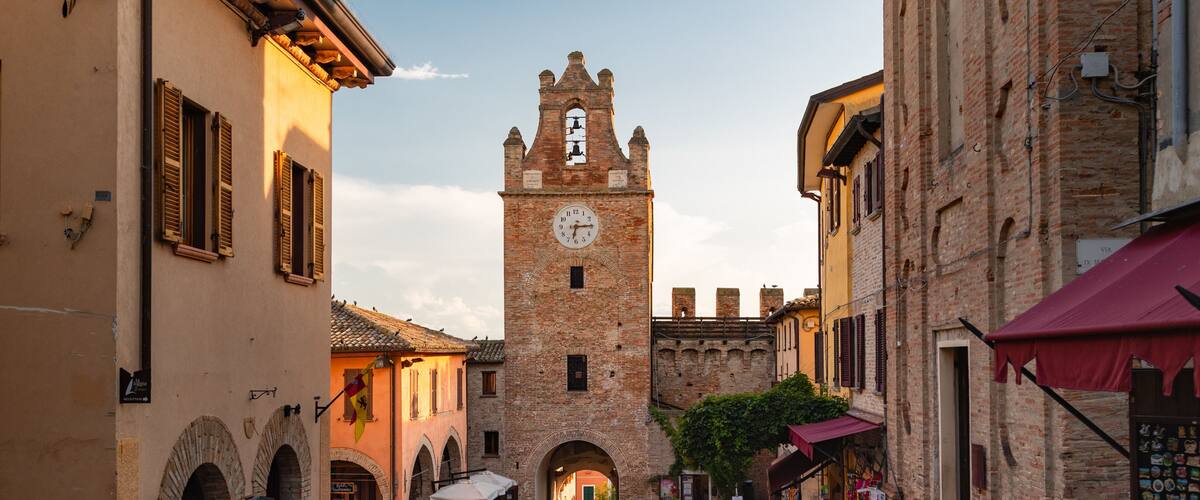A cobblestone street with historic buildings, a clock tower, and people walking.