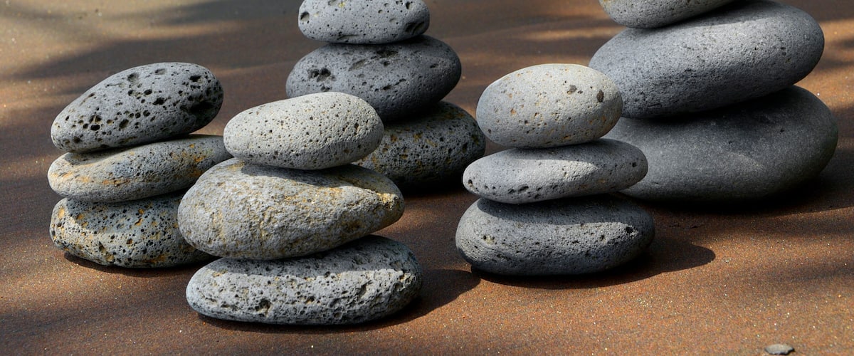 A stack of smooth, rounded stones on a sandy beach with shadows of trees in the background.