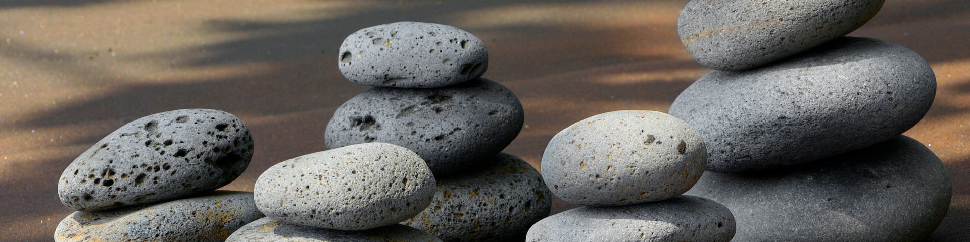 A stack of smooth, rounded stones on a sandy beach with shadows of trees in the background.