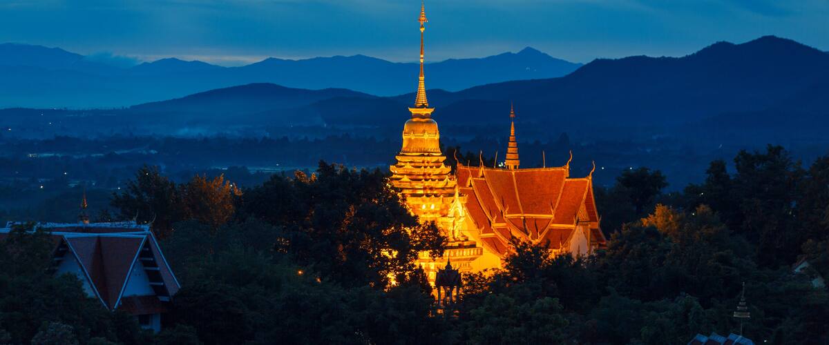 A golden pagoda at dusk with mountains in the background.