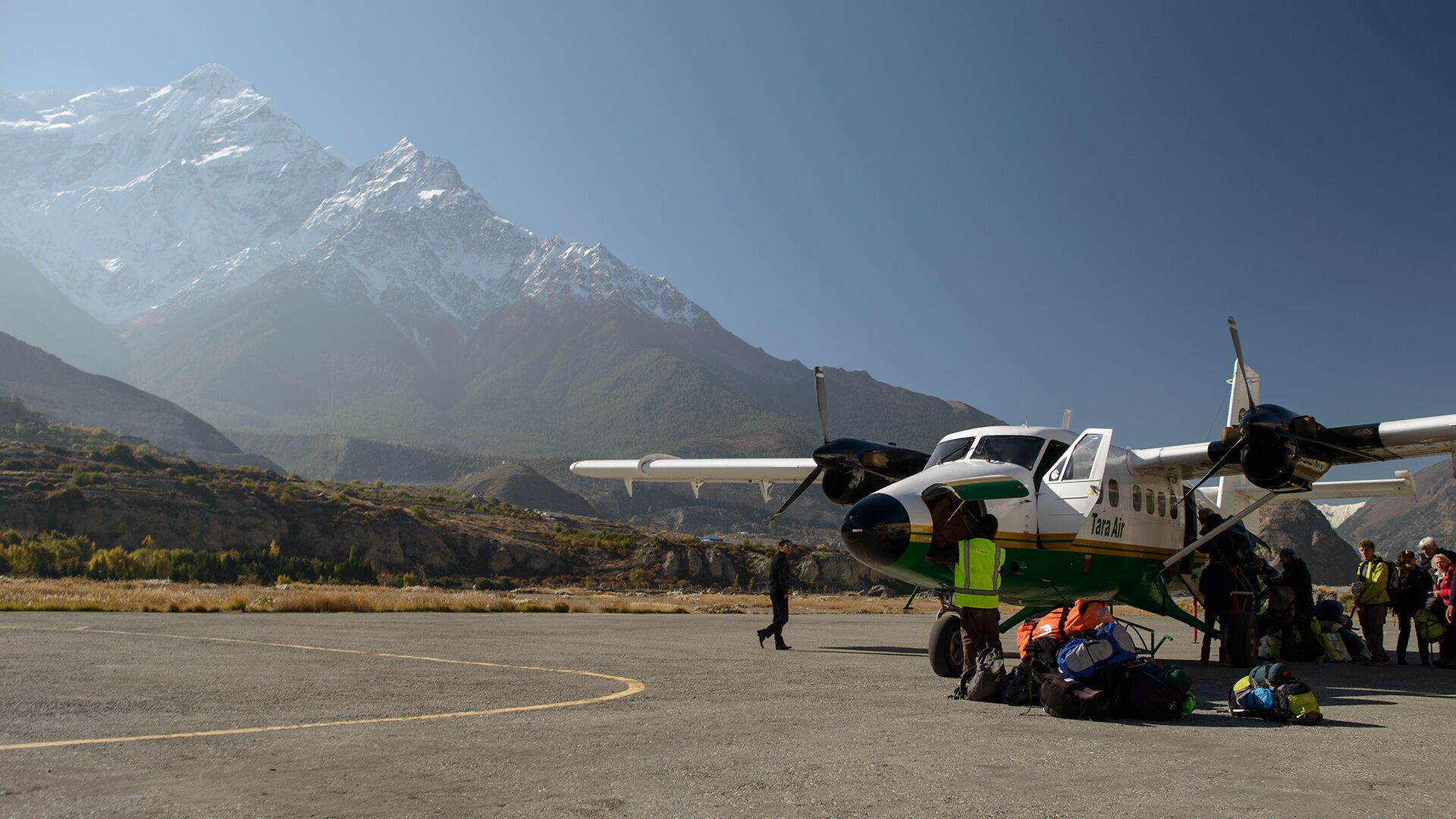 A small propeller plane on a tarmac with a mountainous backdrop.