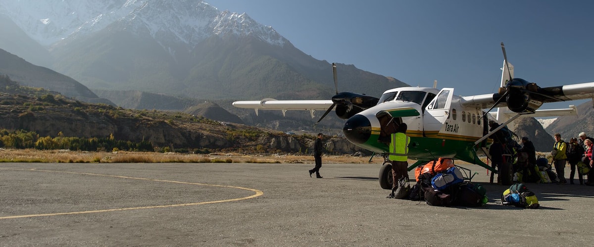A small propeller plane on a tarmac with a mountainous backdrop.