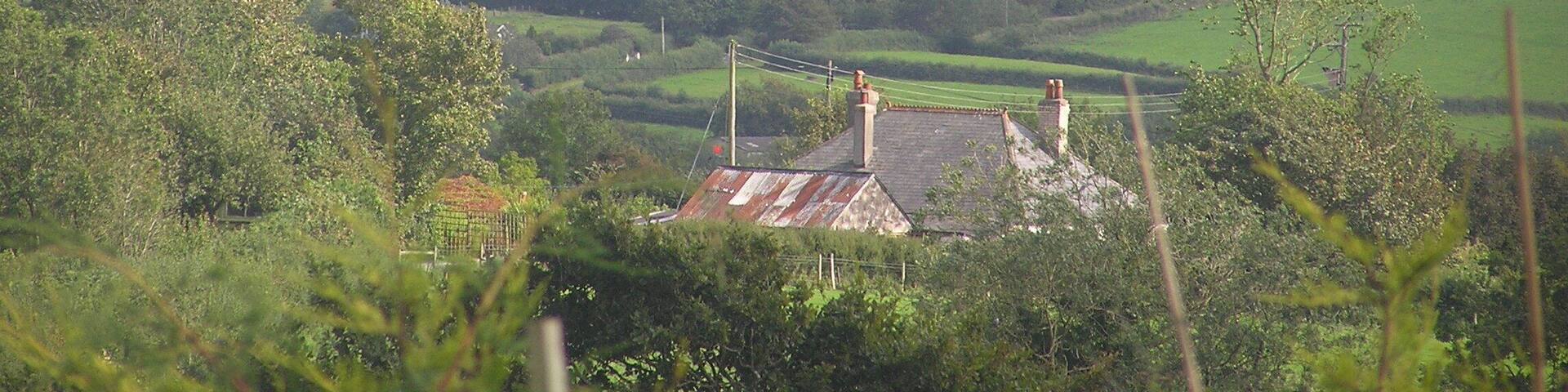 A rural landscape with rolling hills, a small house with a thatched roof, and a distant mountain range.