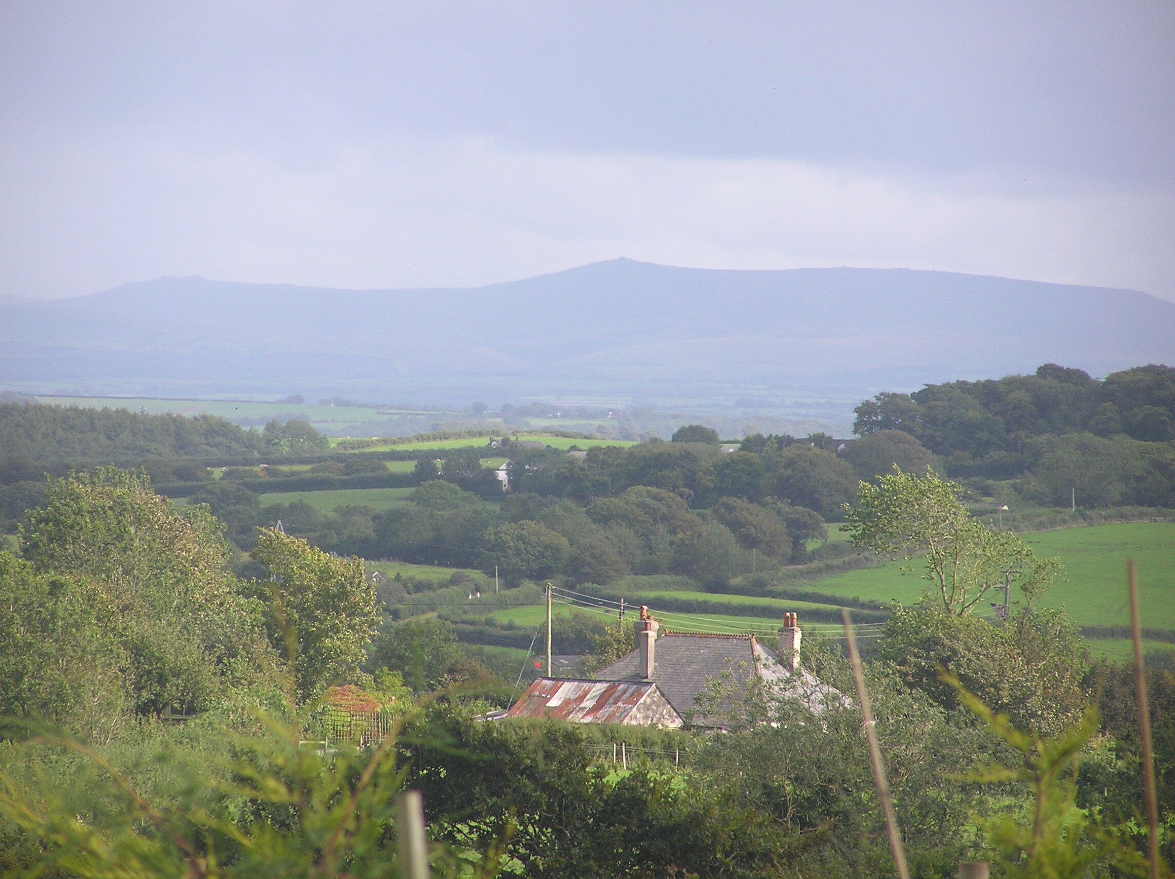 A rural landscape with rolling hills, a small house with a thatched roof, and a distant mountain range.