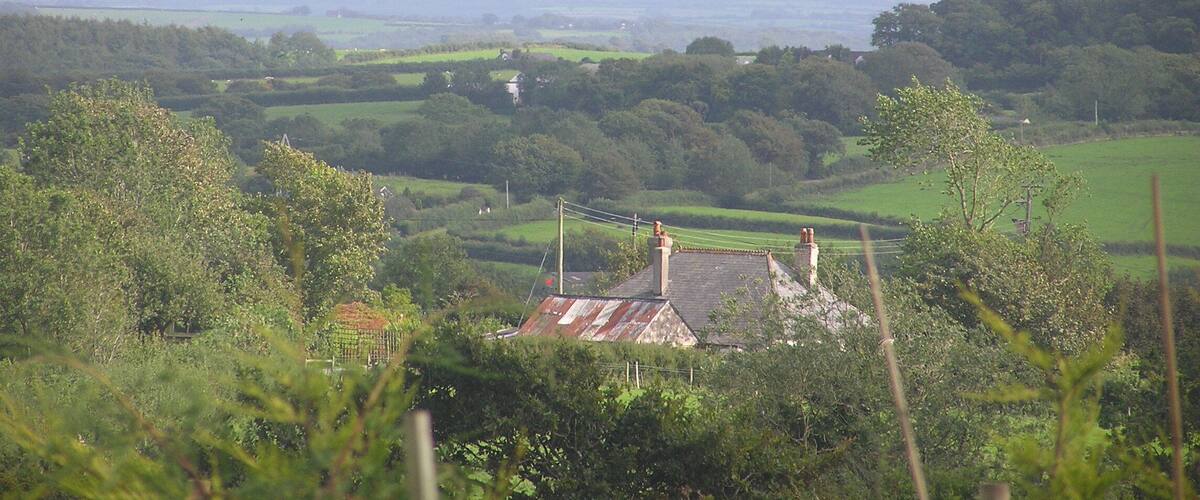 A rural landscape with rolling hills, a small house with a thatched roof, and a distant mountain range.