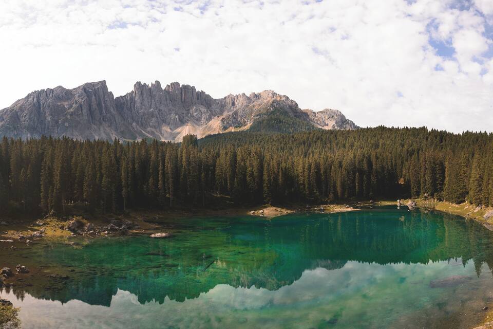 Ein klarer See, umgeben von dichtem Wald und zerklüfteten Bergen.