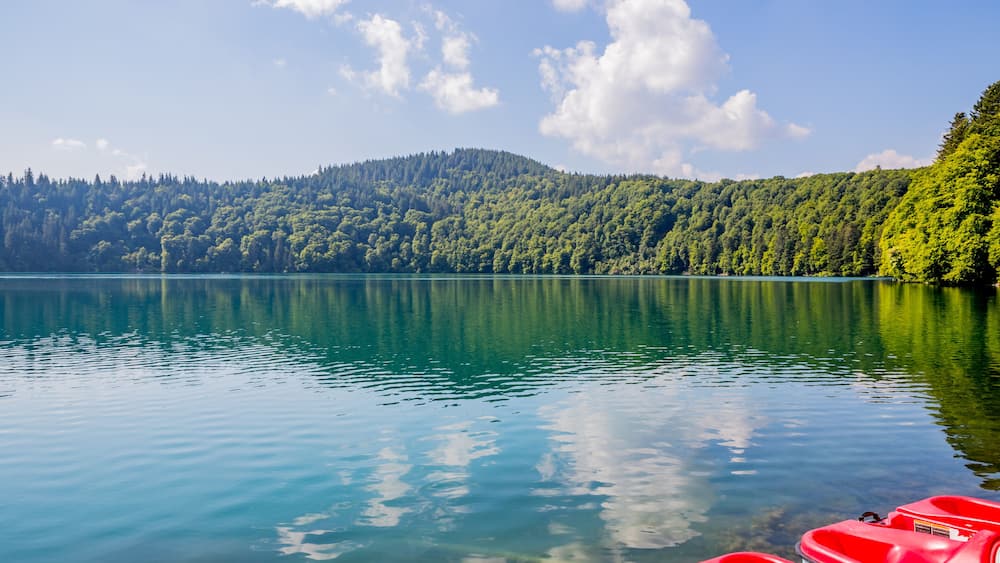 Un lac paisible aux eaux claires, où le ciel et la forêt environnante se reflètent.