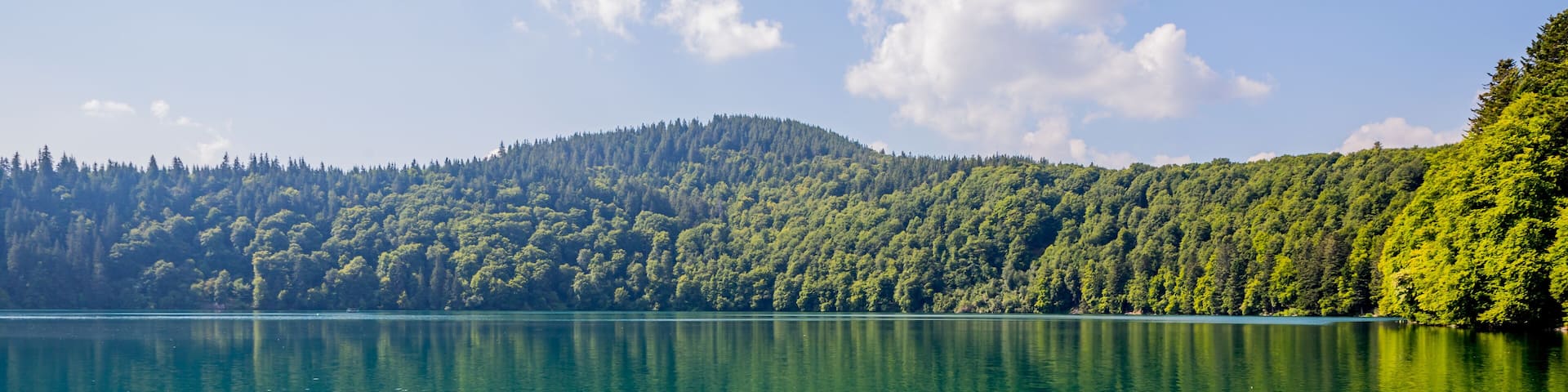 A calm lake with clear water reflecting the sky and surrounding forest.