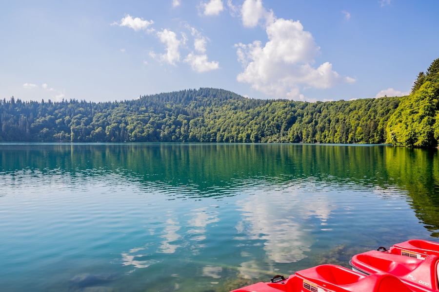 Ein ruhiger See mit klarem Wasser, das den Himmel und den umliegenden Wald spiegelt.