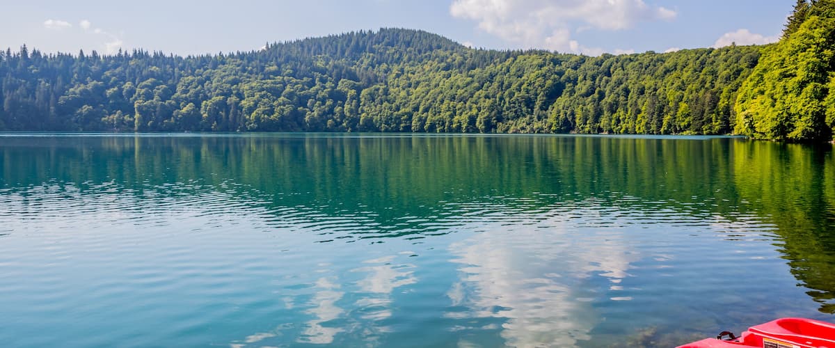 A calm lake with clear water reflecting the sky and surrounding forest.