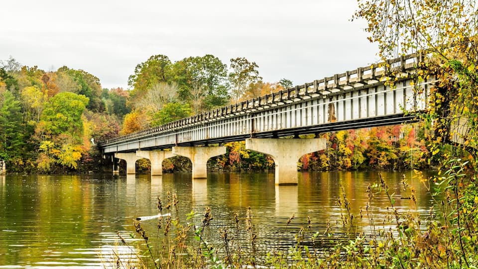 A bridge over a calm river surrounded by autumn foliage.
