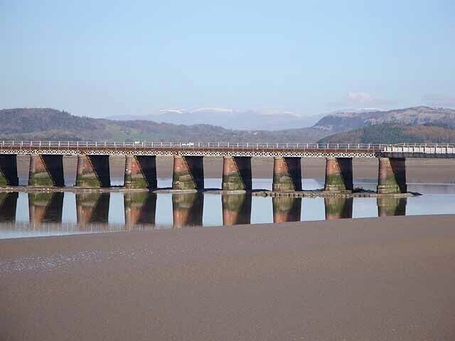 A bridge over a calm river with mountains in the background.