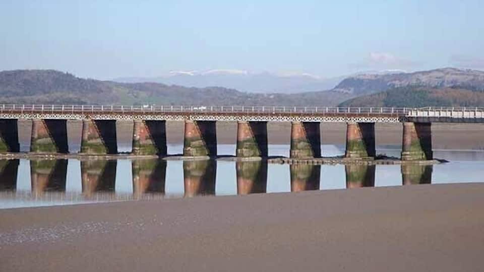 A bridge over a calm river with mountains in the background.