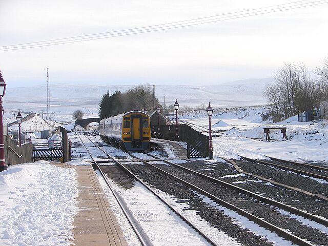 A train on tracks with snow on the ground and a bridge in the background.
