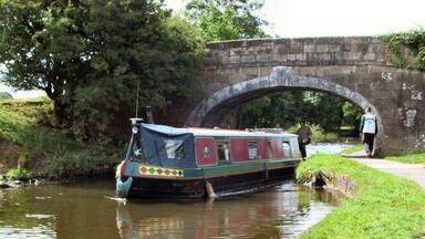 A narrowboat on a river, a stone bridge, and a grassy bank.