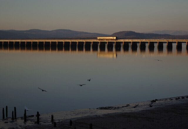 A bridge over calm water with mountains in the background.
